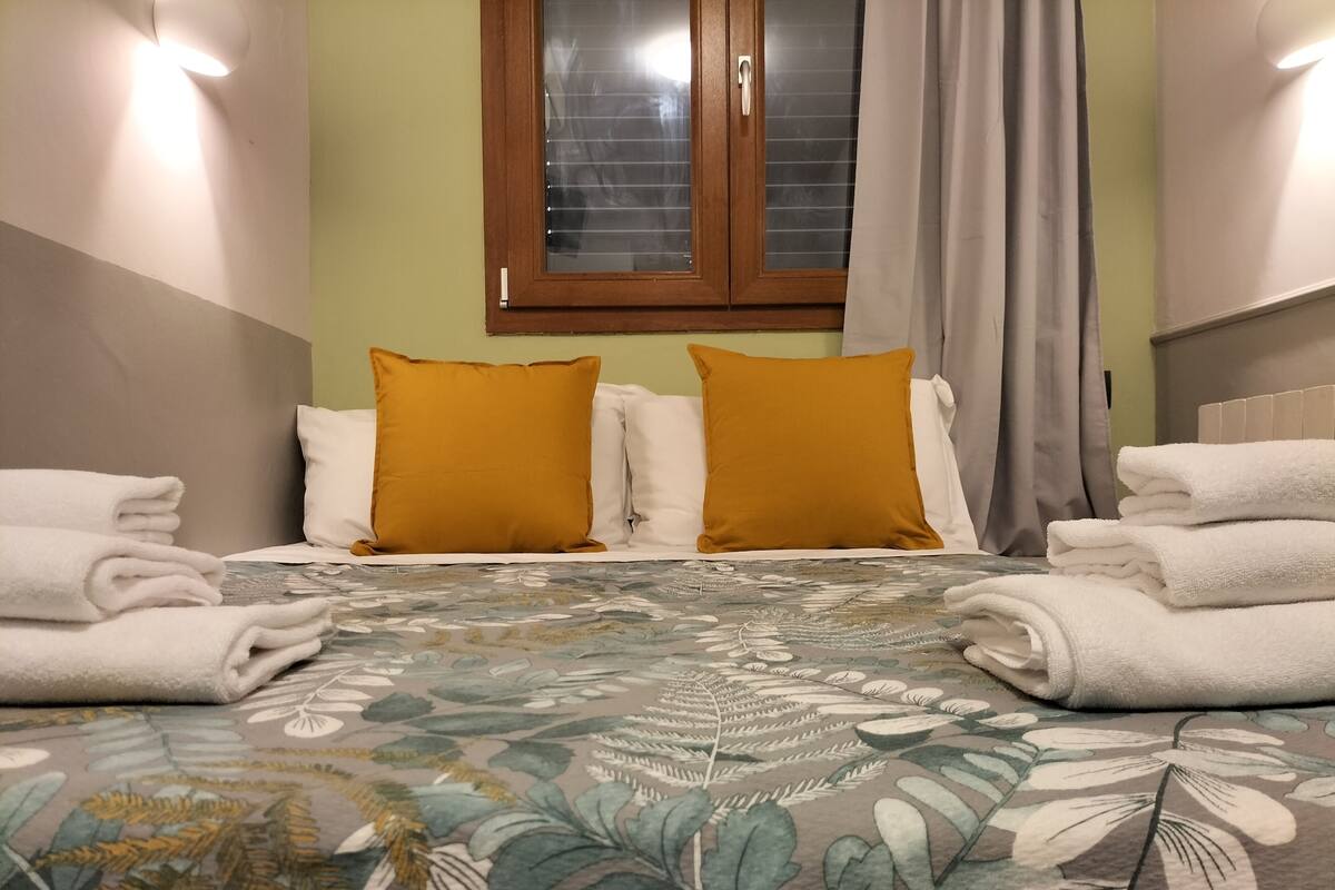 Una habitación de hotel con una cama, dos almohadas, un ventanal y una cortina.