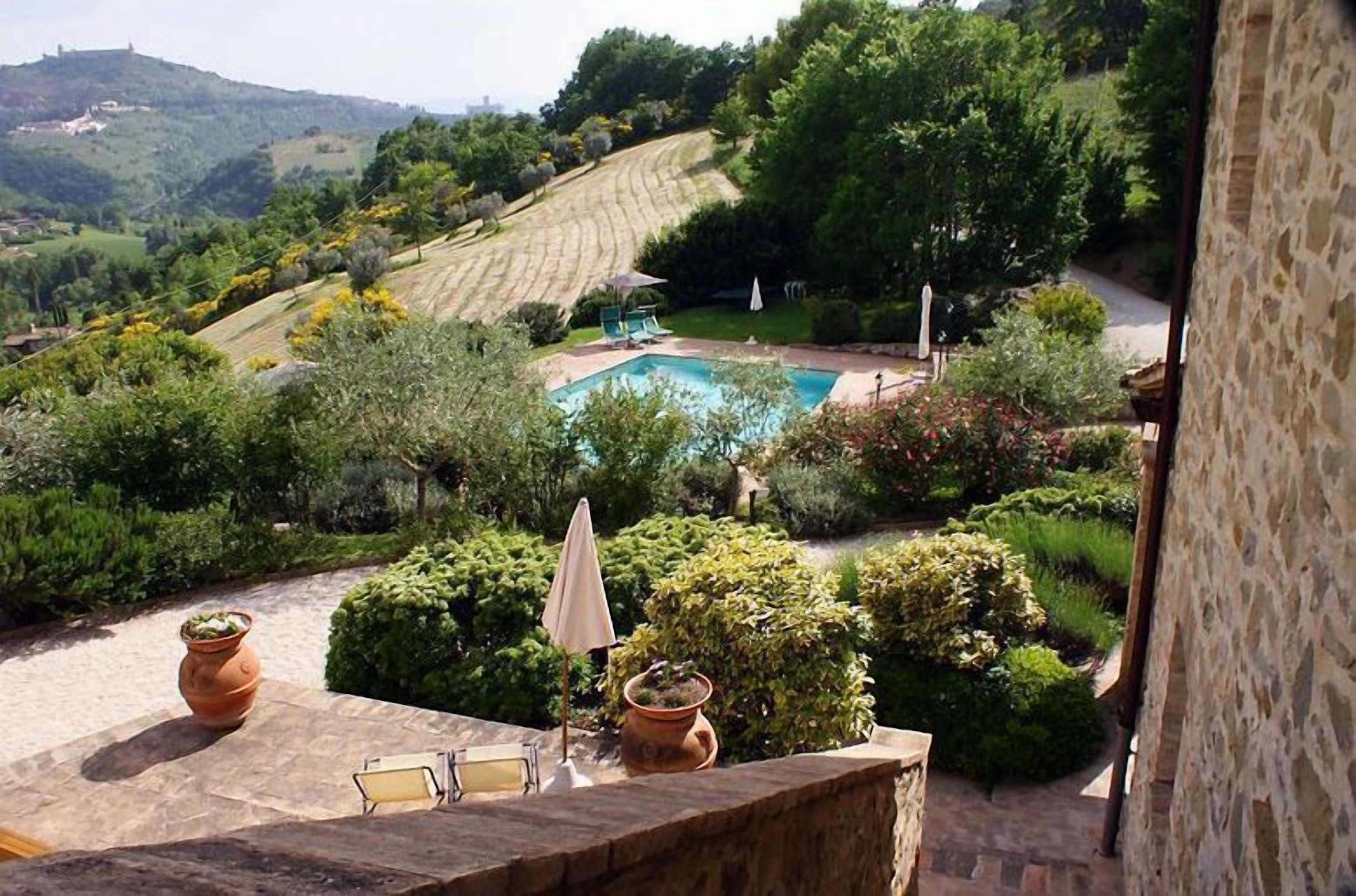 Área da piscina com vista para vinhedos em socalcos, muros de pedra e plantas em vasos.