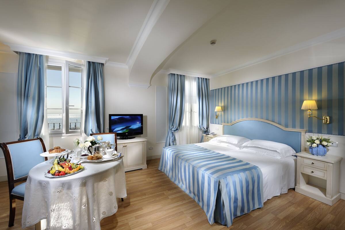 Ett hotellrum med en säng, en TV, ett matbord med frukost och utsikt över staden.