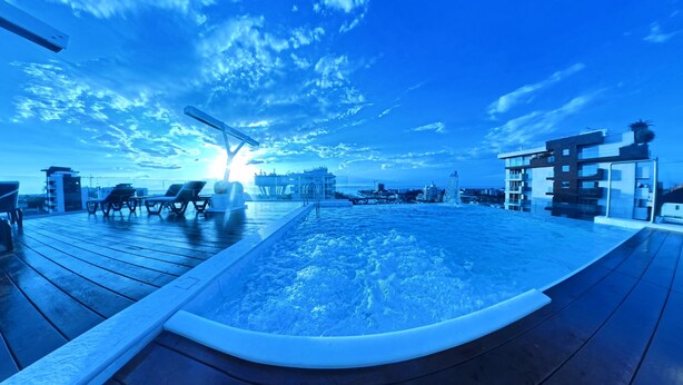 Una piscina infinita en la azotea con sillones de descanso y vistas al horizonte de la ciudad.