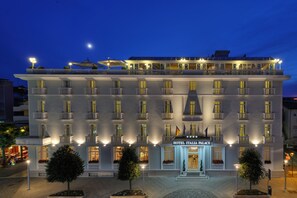Un hotel de varios pisos con un balcón en el piso superior, una entrada bien iluminada y un letrero que dice "HOTEL ITALIA PALACE".