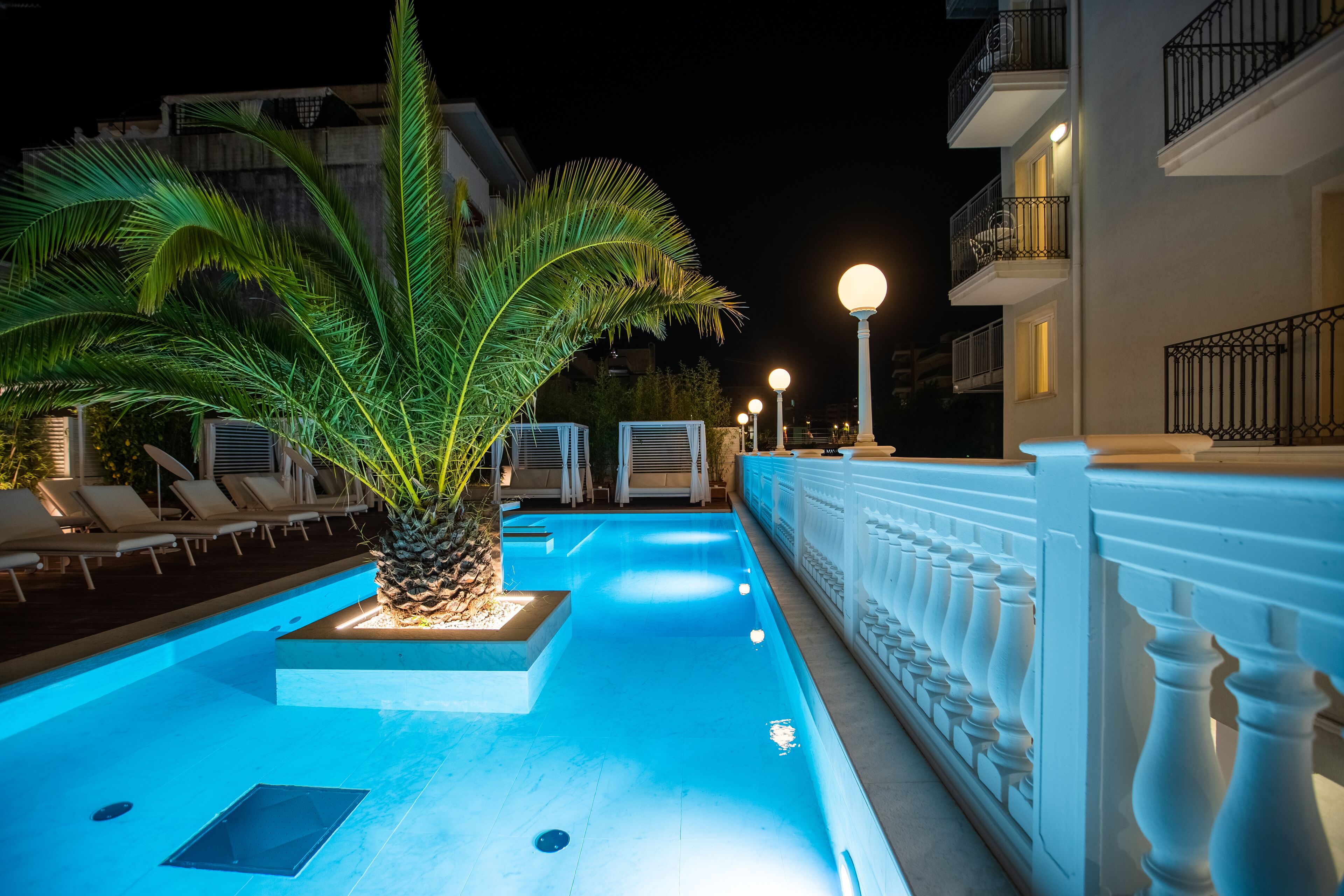 Ein Swimmingpool mit einer Palme, Liegestühlen und einer weißen Brüstung.