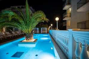 Una piscina con una palmera, sillas de descanso y una barandilla blanca.