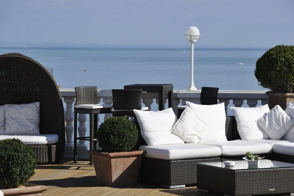 A deck with a sofa, chairs, and a table, overlooking a body of water.