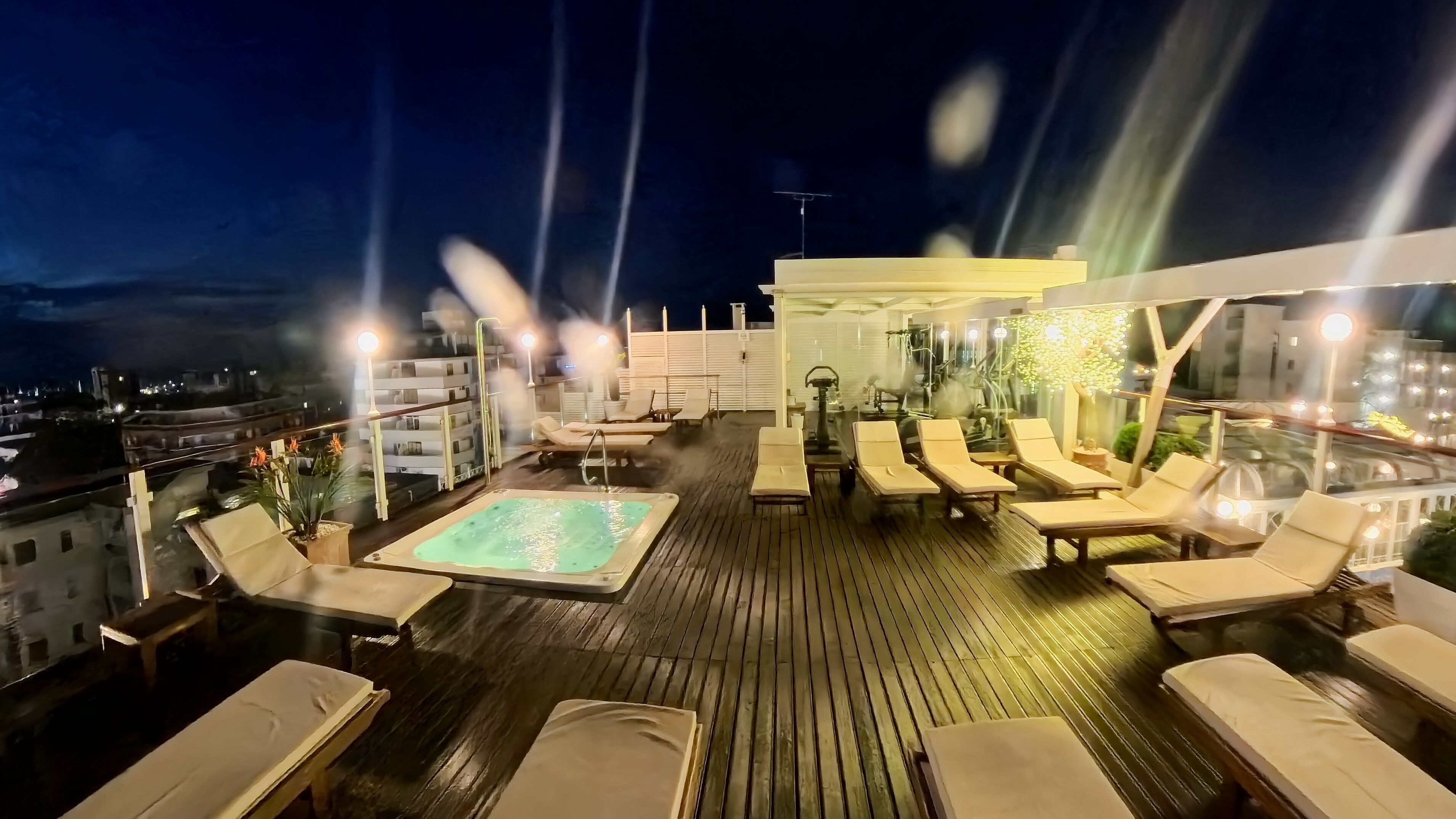 Una terraza en la azotea con piscina, sillones de descanso y un espacio de estar cubierto.