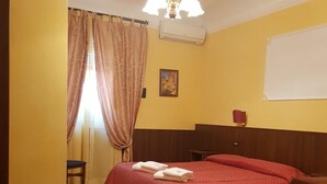 A hotel room with a bed, a chair, a window with curtains, a chandelier, and a wall-mounted air conditioner. - Rudy B&B (Rome)