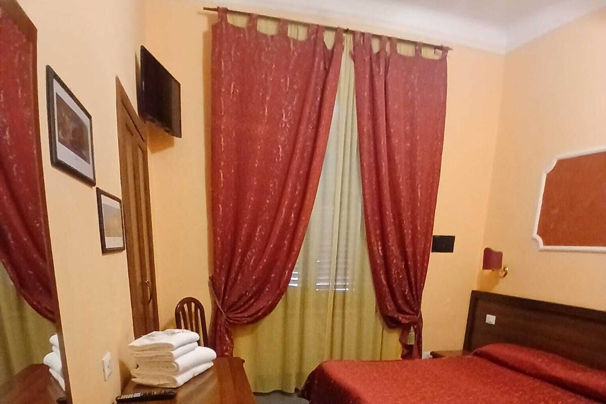 Une chambre d’hôtel avec un lit, un bureau, une chaise et un téléviseur fixé au mur.