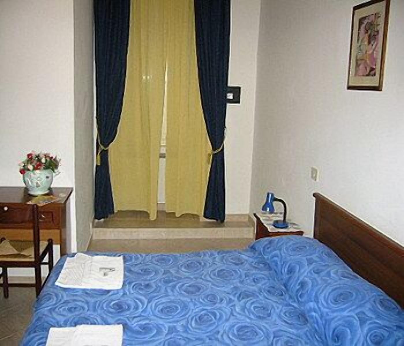 Habitación de hotel con cama, escritorio, silla, mesita de noche, lámpara y un cuadro en la pared.