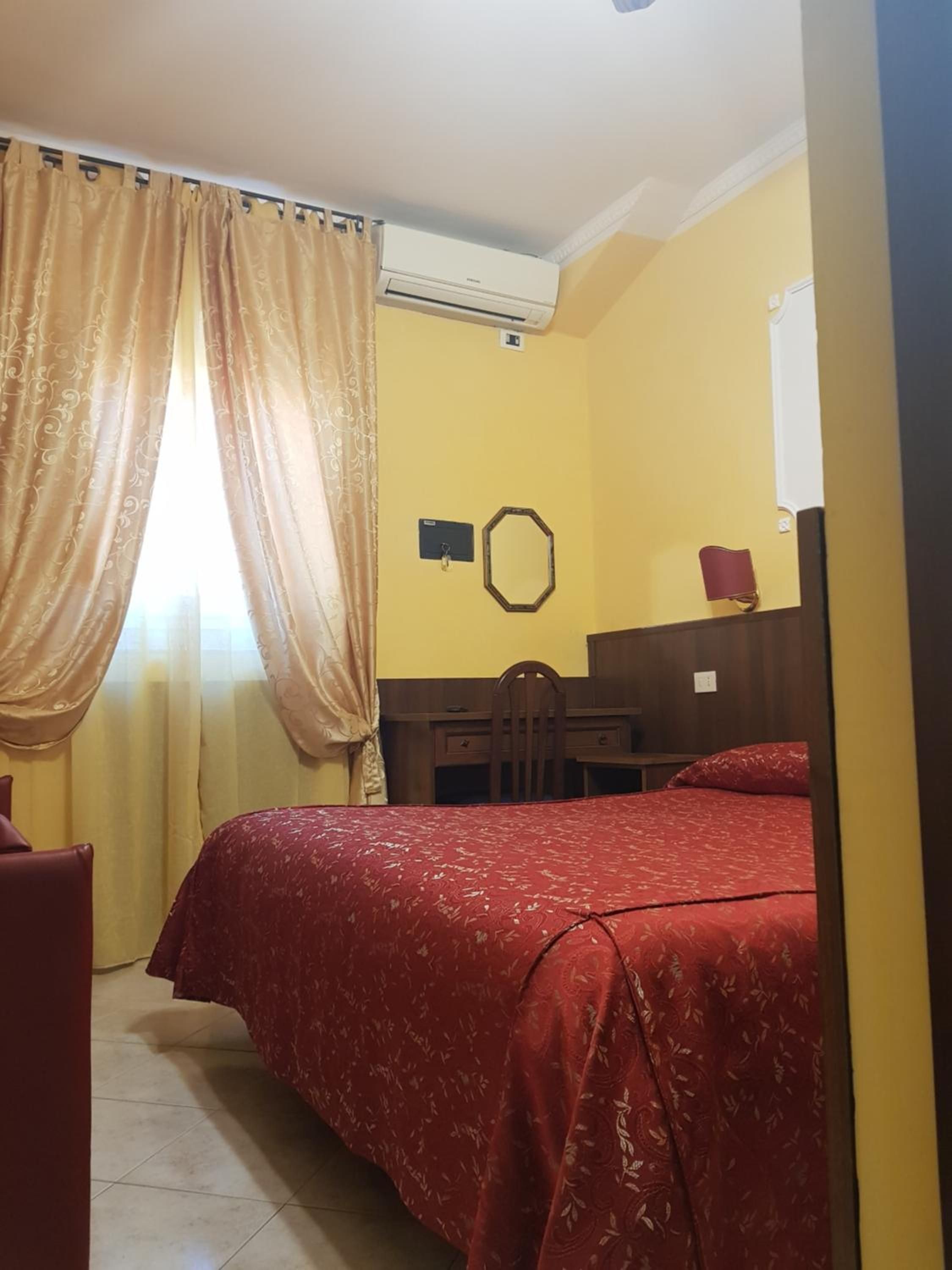 A room with a bed, a desk, and a chair. There is an air conditioning unit on the wall.
