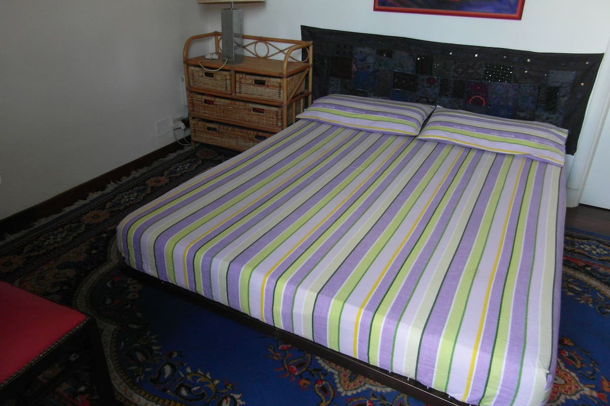 A bed with striped bedding, a headboard, and a wall-mounted lamp.
