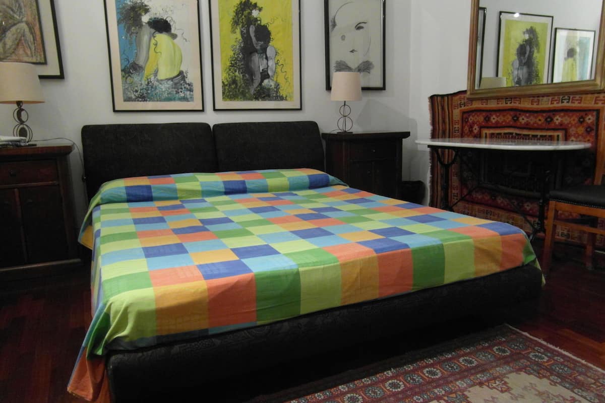 A bedroom with a large bed, a nightstand, a lamp, and a mirror.