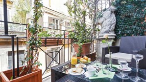 An outdoor dining area with wicker furniture, a stone sculpture, and potted plants. - Pantheonview - Luxury Suites (Rome)