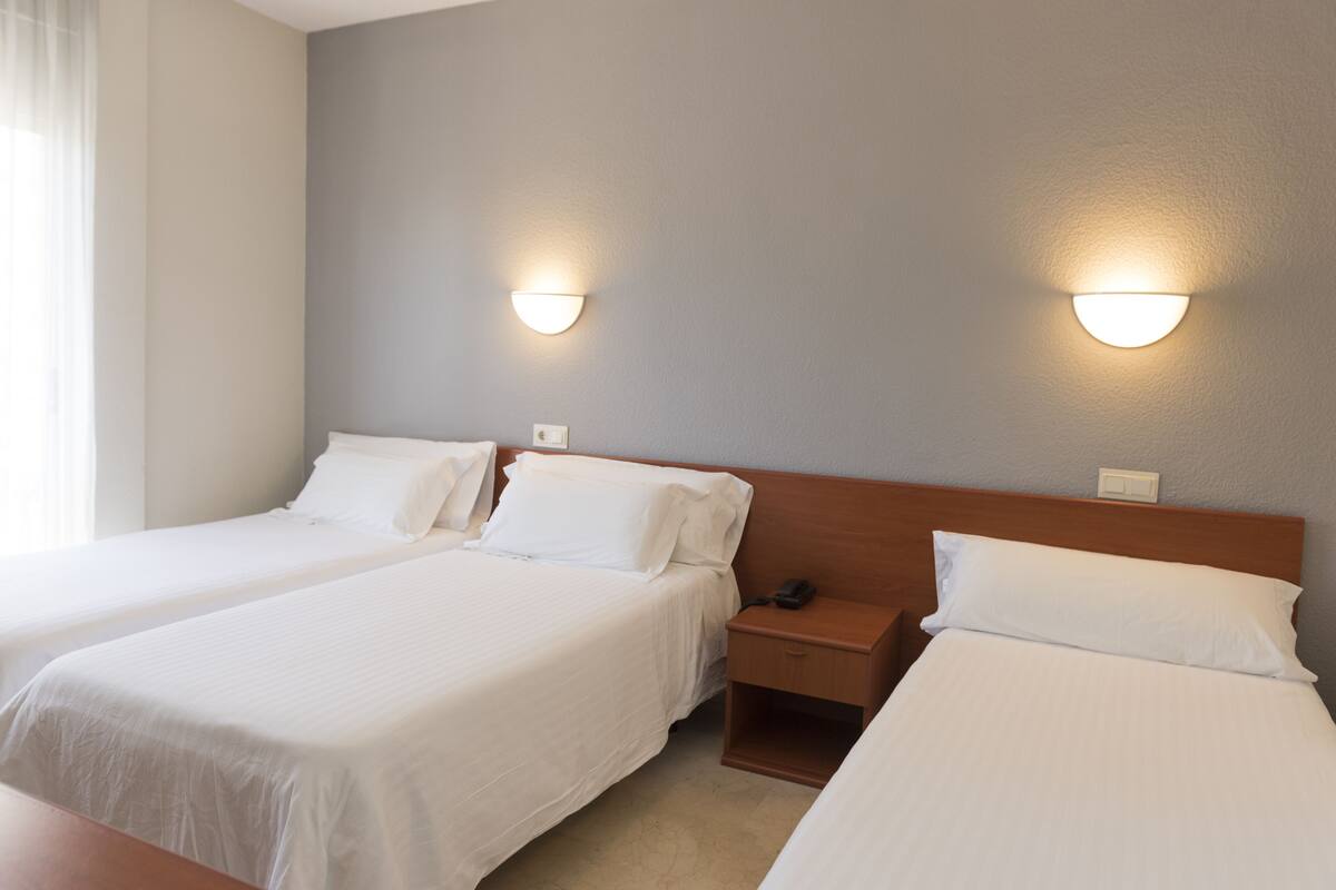 Quarto de hotel com duas camas de solteiro, cabeceira de madeira, mesas de cabeceira e luminárias fixadas na parede.