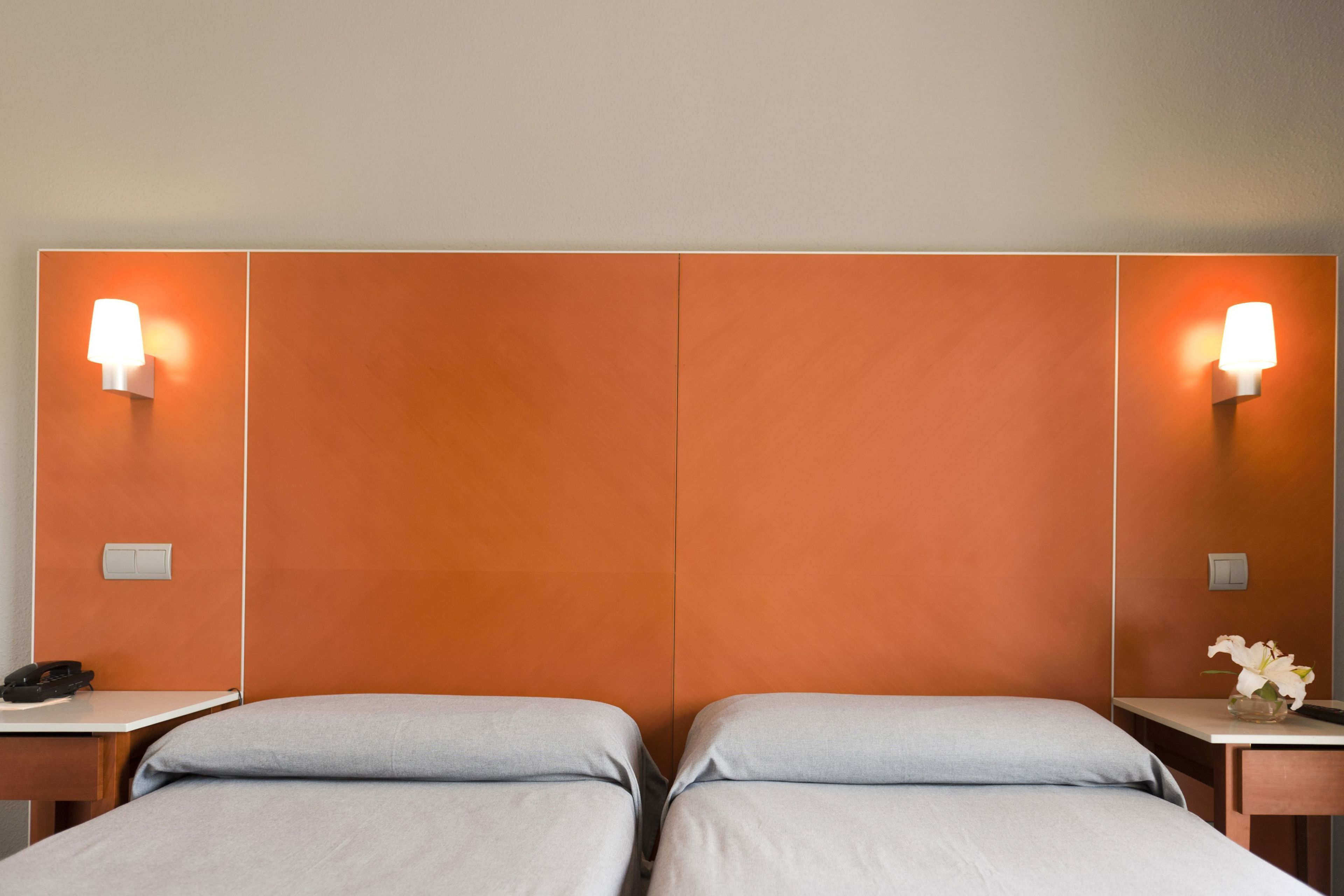 Una habitación de hotel con dos camas, una mesita de noche con teléfono y lámparas de pared.