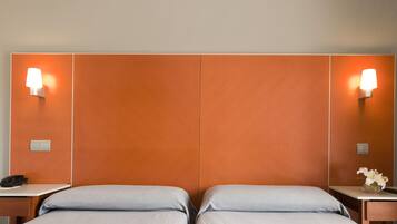 Una habitación de hotel con dos camas, una mesita de noche con teléfono y lámparas de pared.