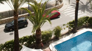 A pool area with palm trees, a road with cars, and a building in the background. - Hotel El Palmeral (Benidorm)