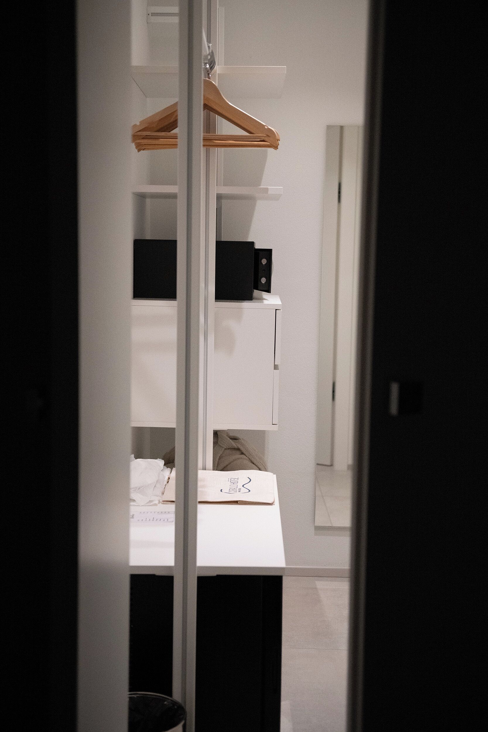 Ein Zimmer mit weißem Schreibtisch, einem an der Wand montierten Kleiderhaken und einem weißen Kleiderschrank.