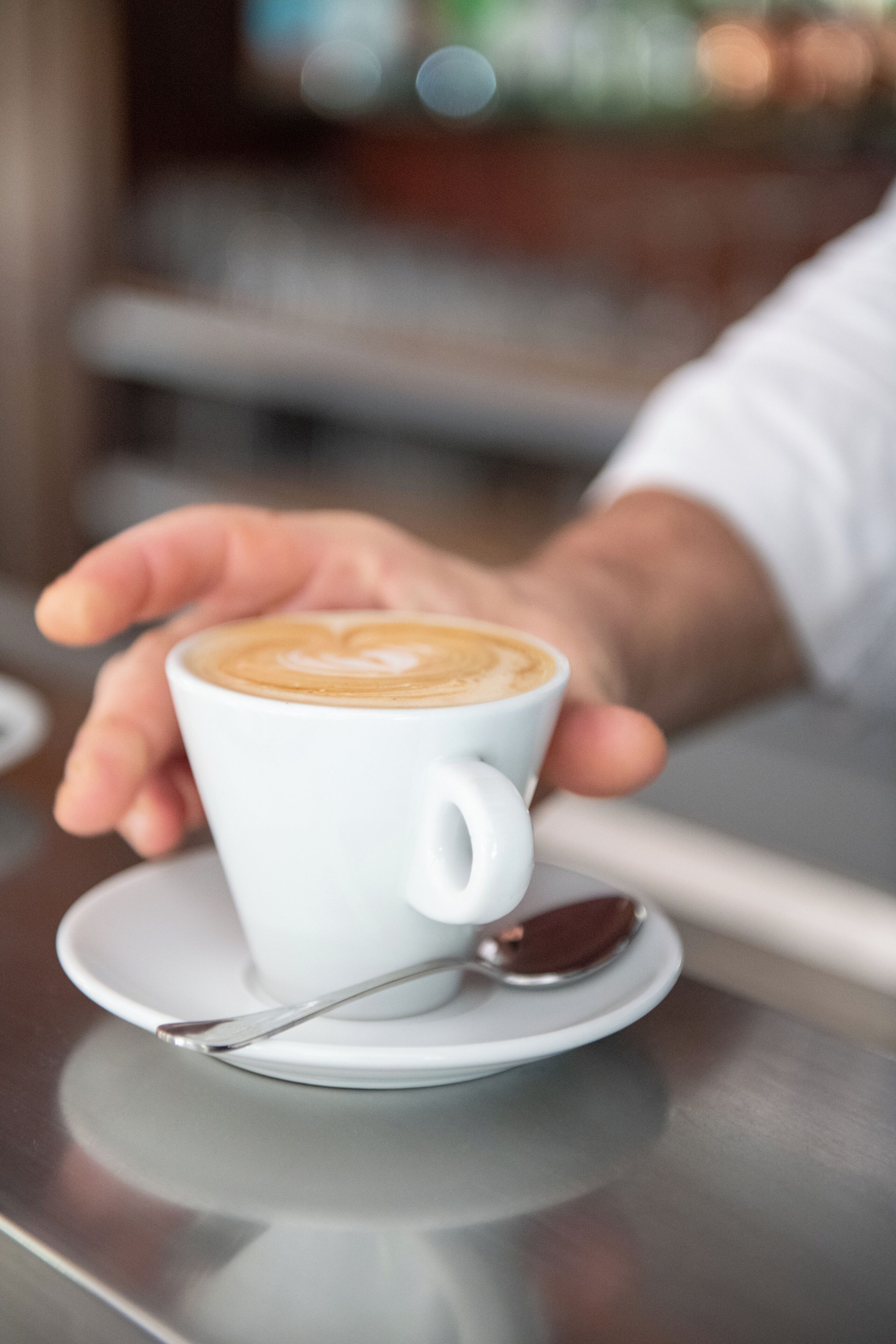 A cup of coffee with latte art on a saucer, held by a hand.