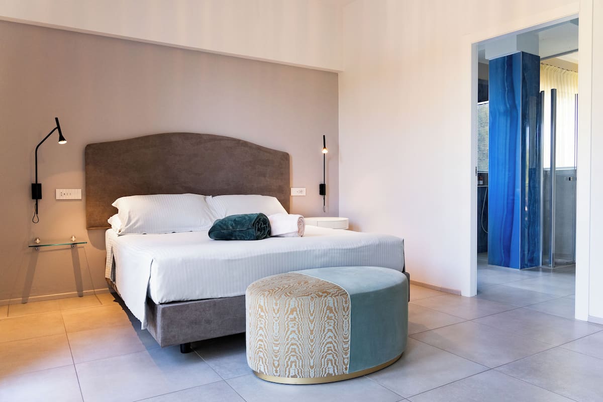 Un dormitorio moderno con una cama grande, lámparas de noche y un pequeño reposapiés.
