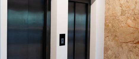 Two elevators in a hallway with a marble wall and a polished floor.