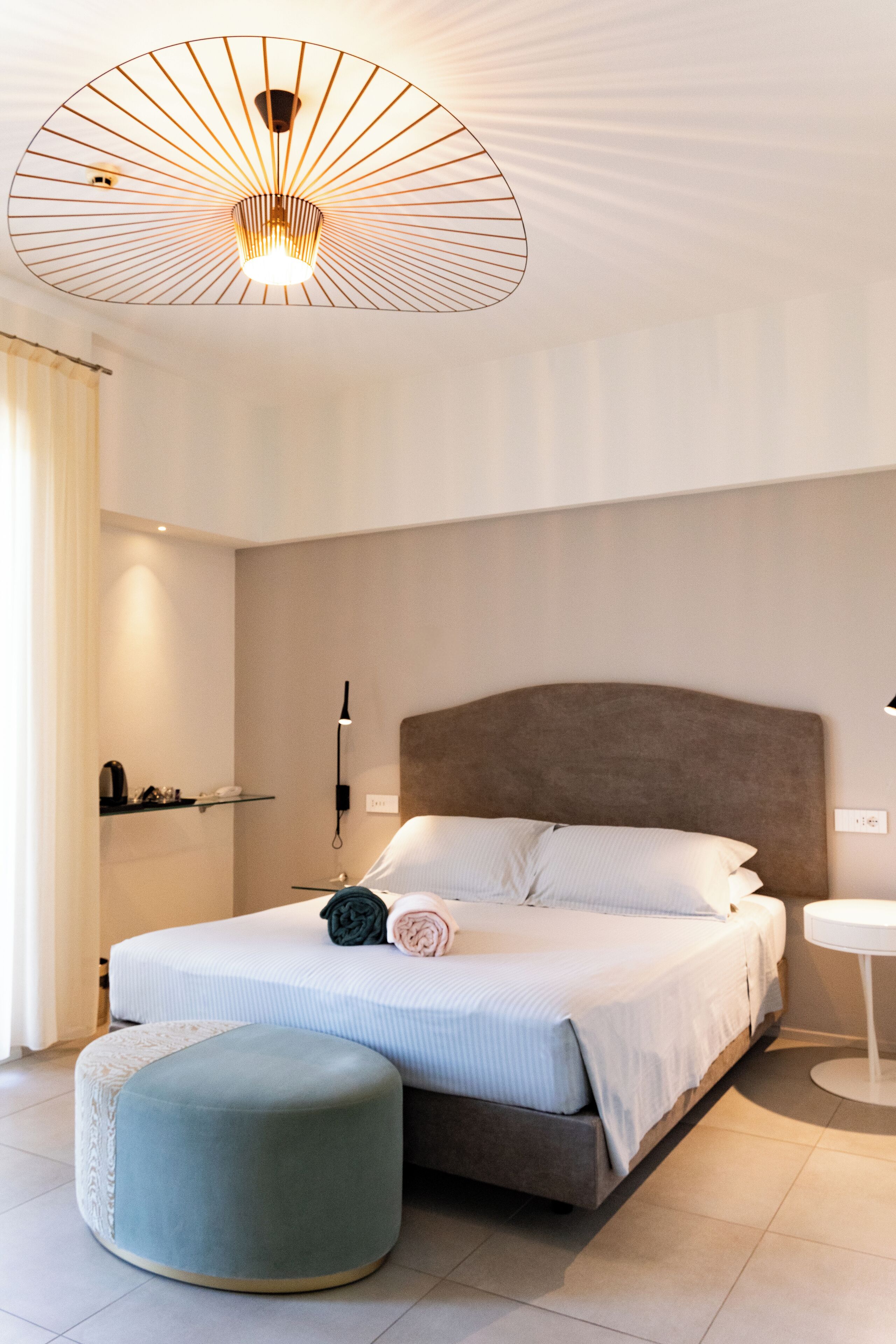 Una camera da letto moderna con un letto grande, comodini, un poggiapiedi rotondo e un lampadario di design.