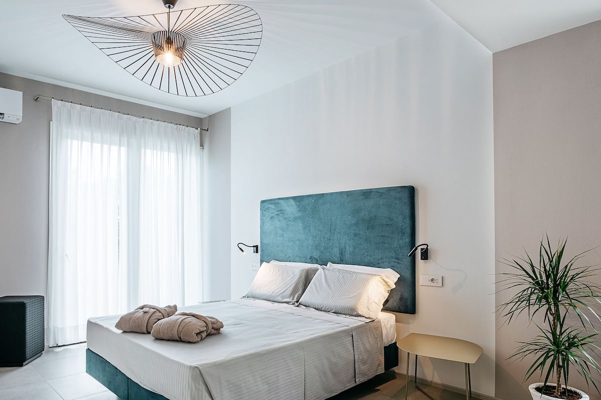Un dormitorio moderno con un cabecero azul aguamarina, una cama con ropa de cama blanca, una mesita de noche y una planta en maceta.