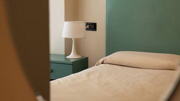 Un letto con una testiera verde e una lampada da comodino bianca in una stanza con una parete color beige.