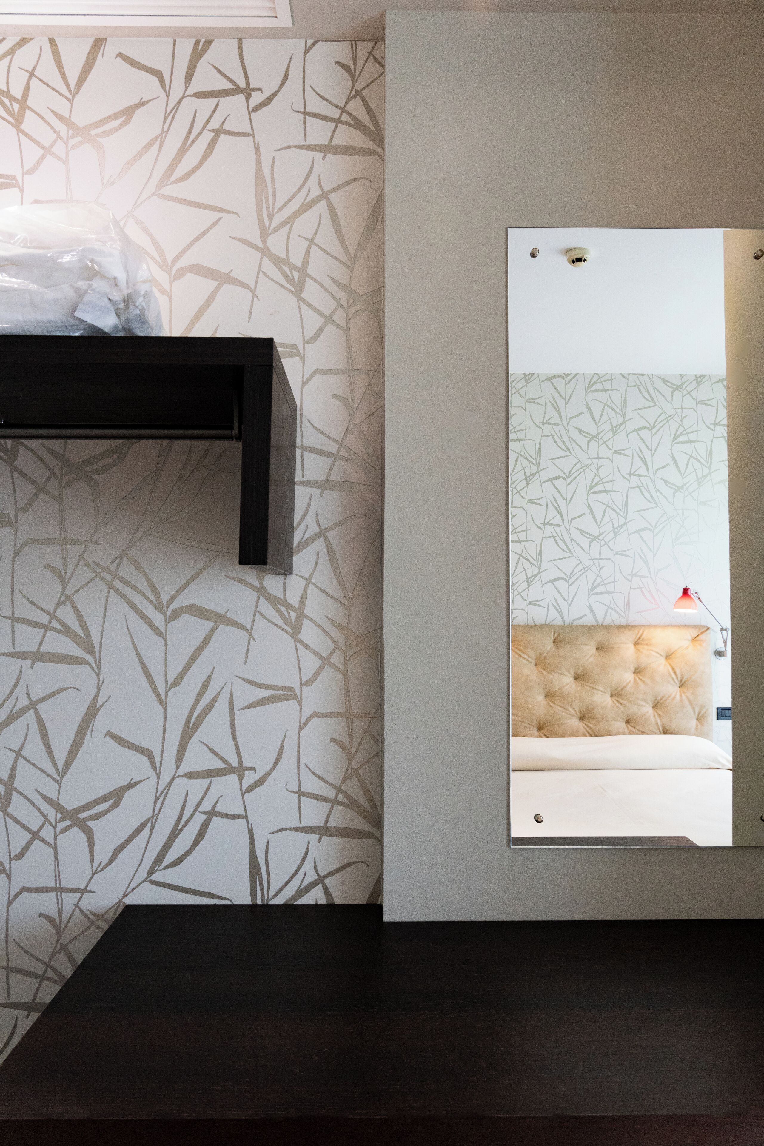 A bathroom with a mirror, a towel rack, and a wall with a bamboo leaf pattern.