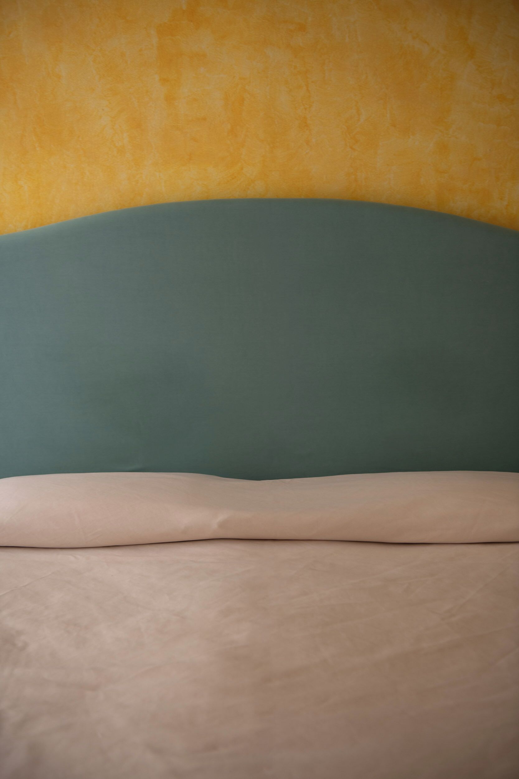 A bed with a green headboard and a beige mattress.