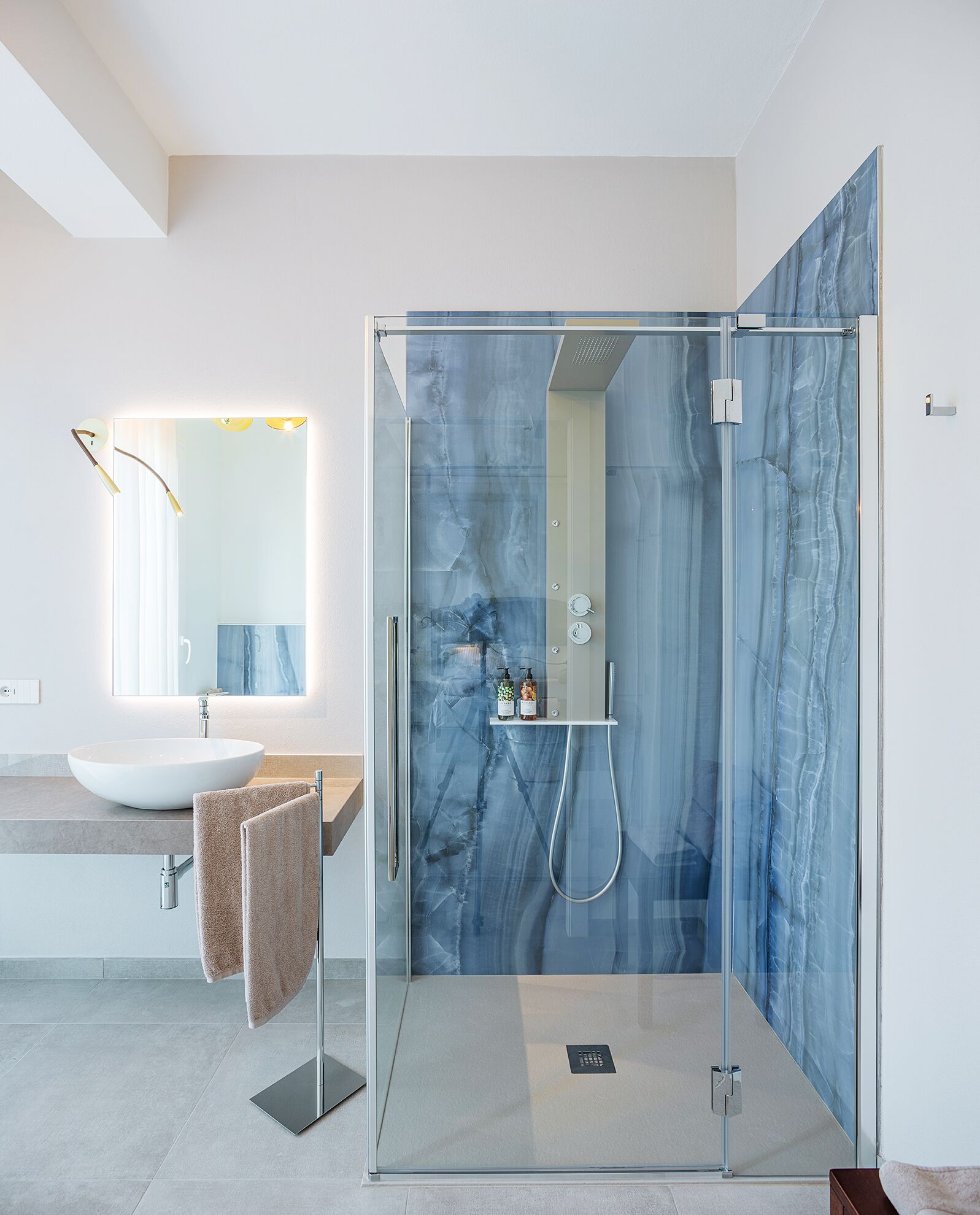 A modern bathroom with a glass-enclosed shower, a white sink, and a large mirror.