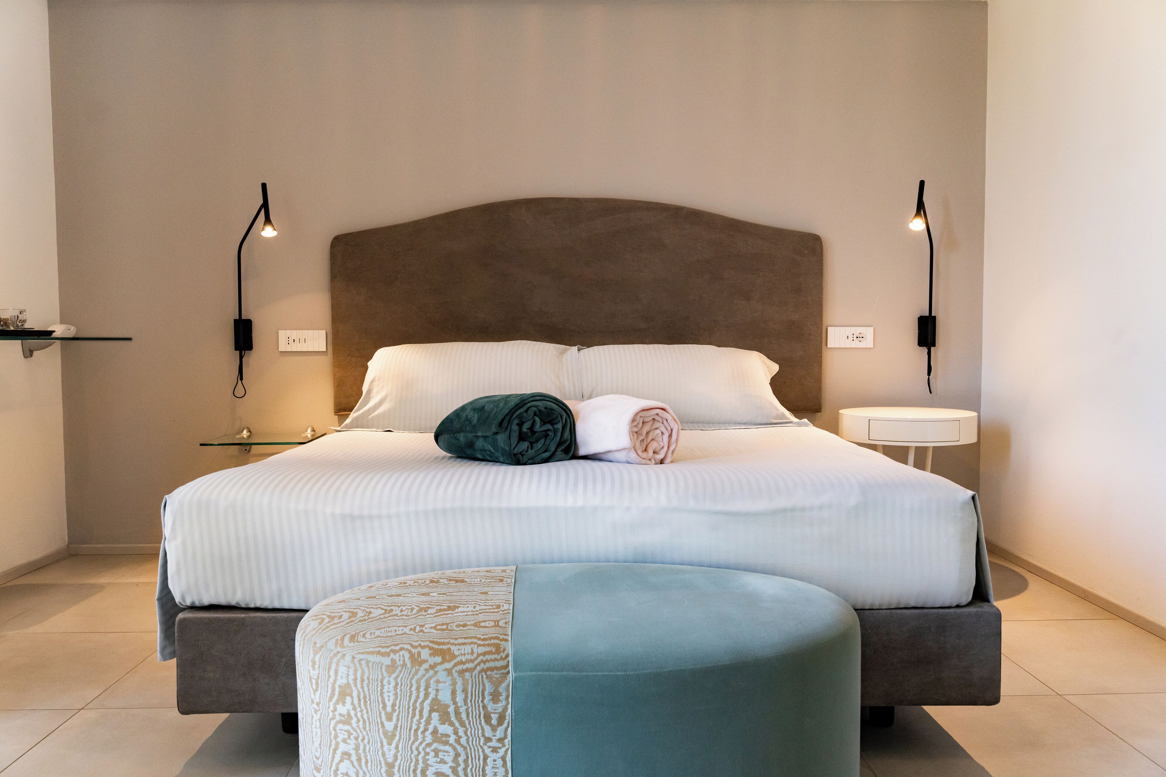 A modern bedroom with a large bed, two bedside lamps, a bedside table, and a small shelf.