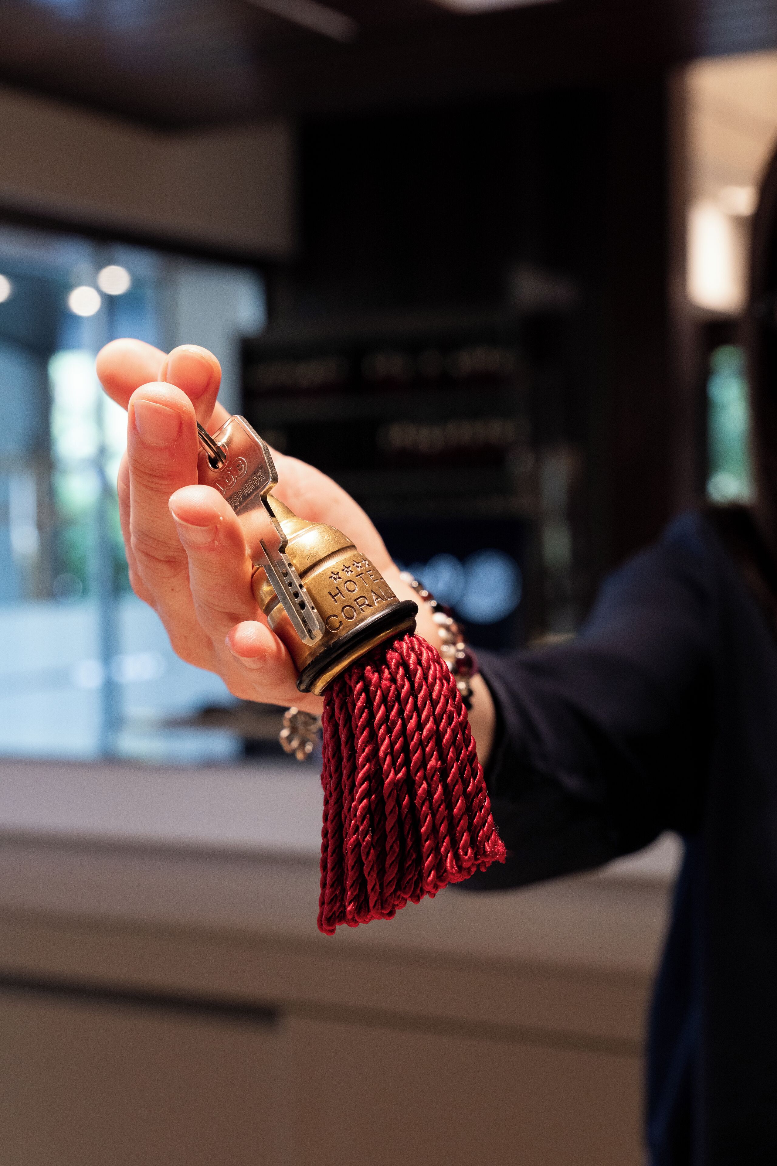 Une main tenant un porte-clés sur lequel est gravé le nom « HOTEL CORAL ».