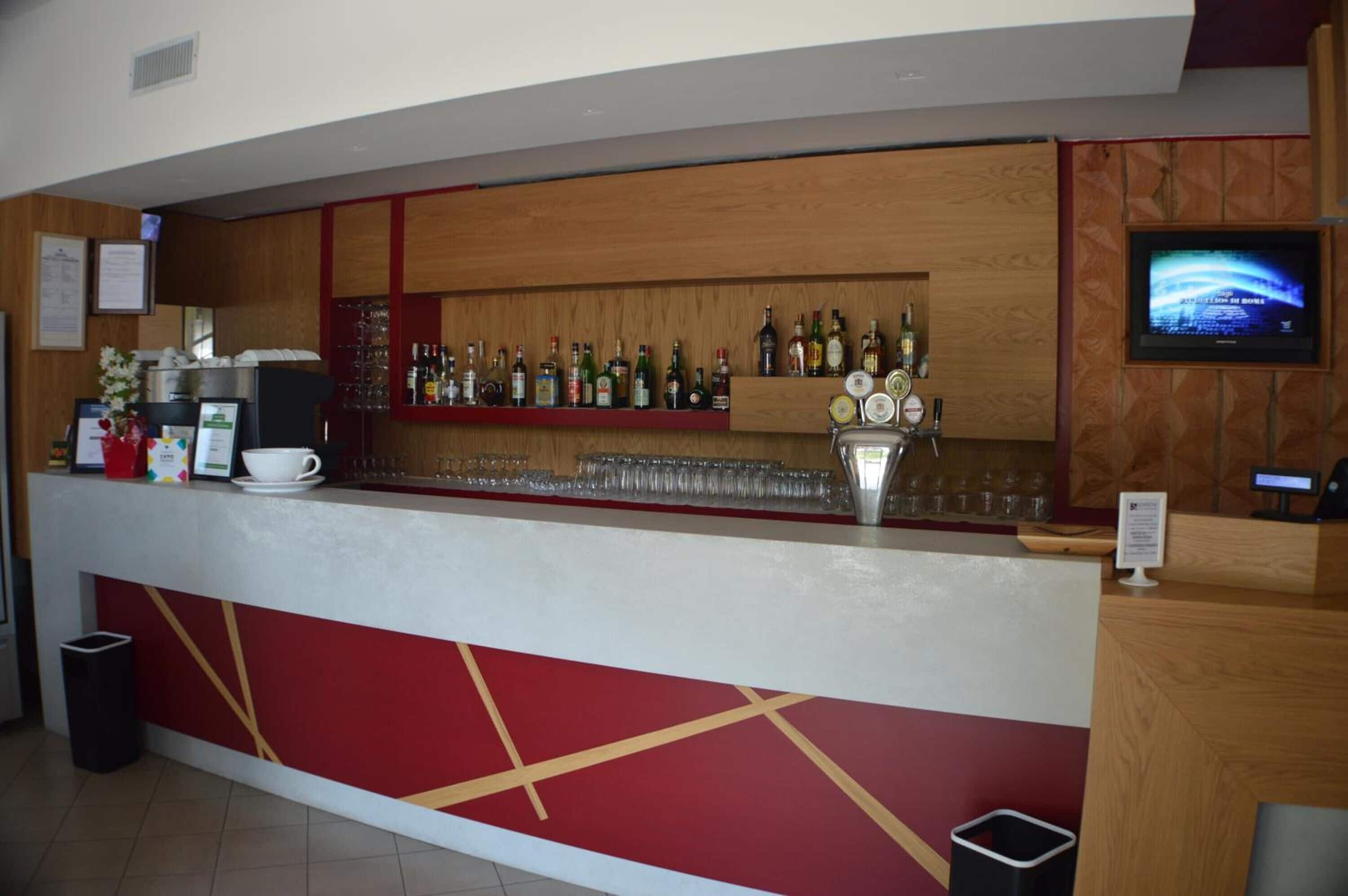 Zona de bar con barra, estantes llenos de botellas de licor, vasos y una pantalla de televisión.