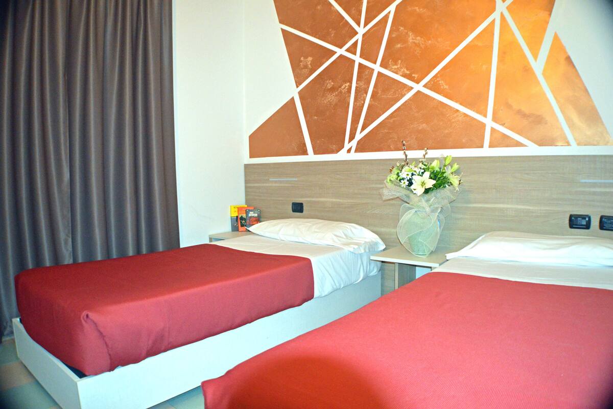 A hotel room with two beds, a nightstand, a vase with flowers, and a geometric wall design.