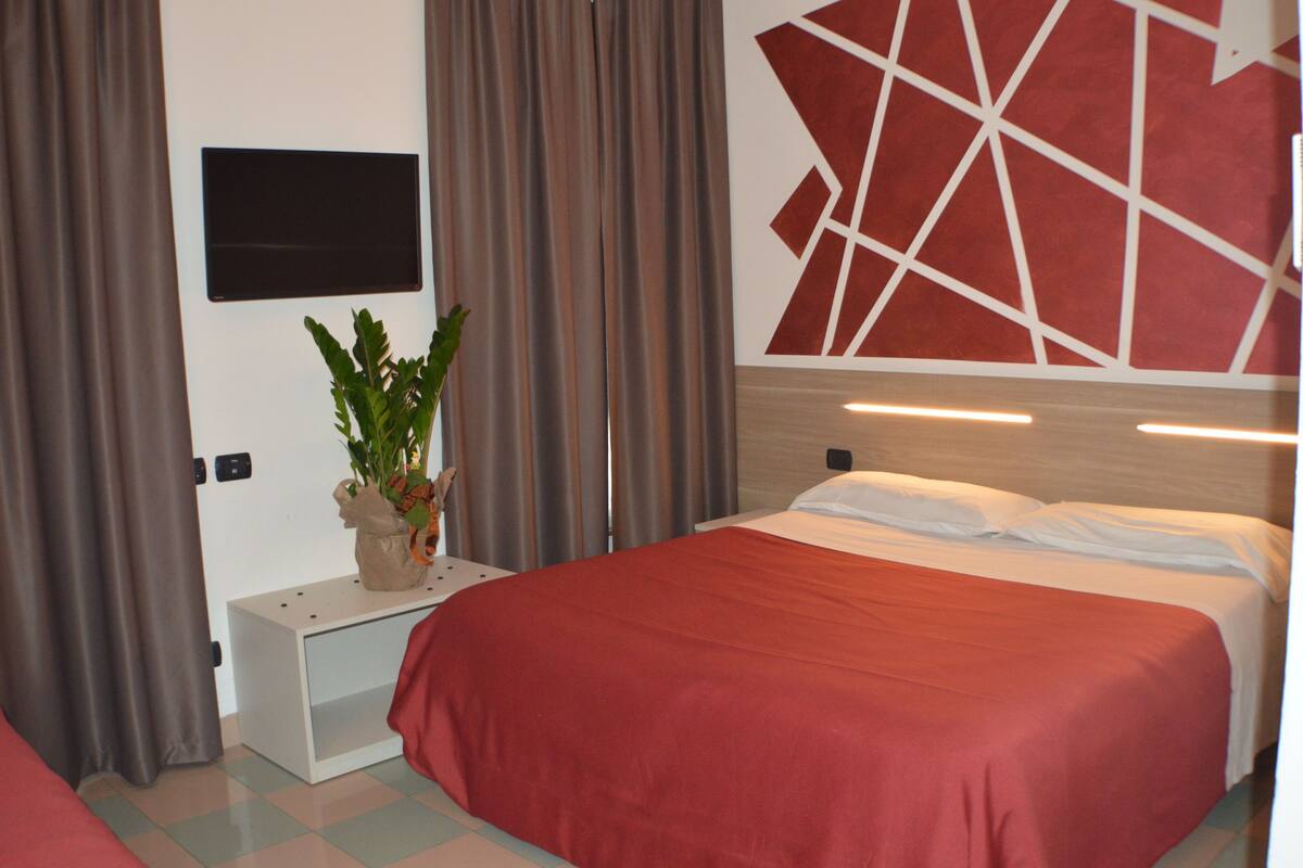 A hotel room with a bed, a bedside table, a wall-mounted TV, and a geometric wall decoration.
