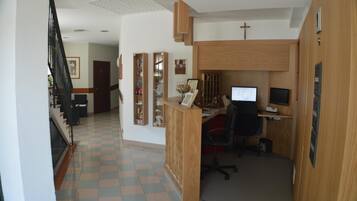 A reception area with a wooden desk, computer, and office chair. There is a staircase on the left and a door at the end of the hallway.