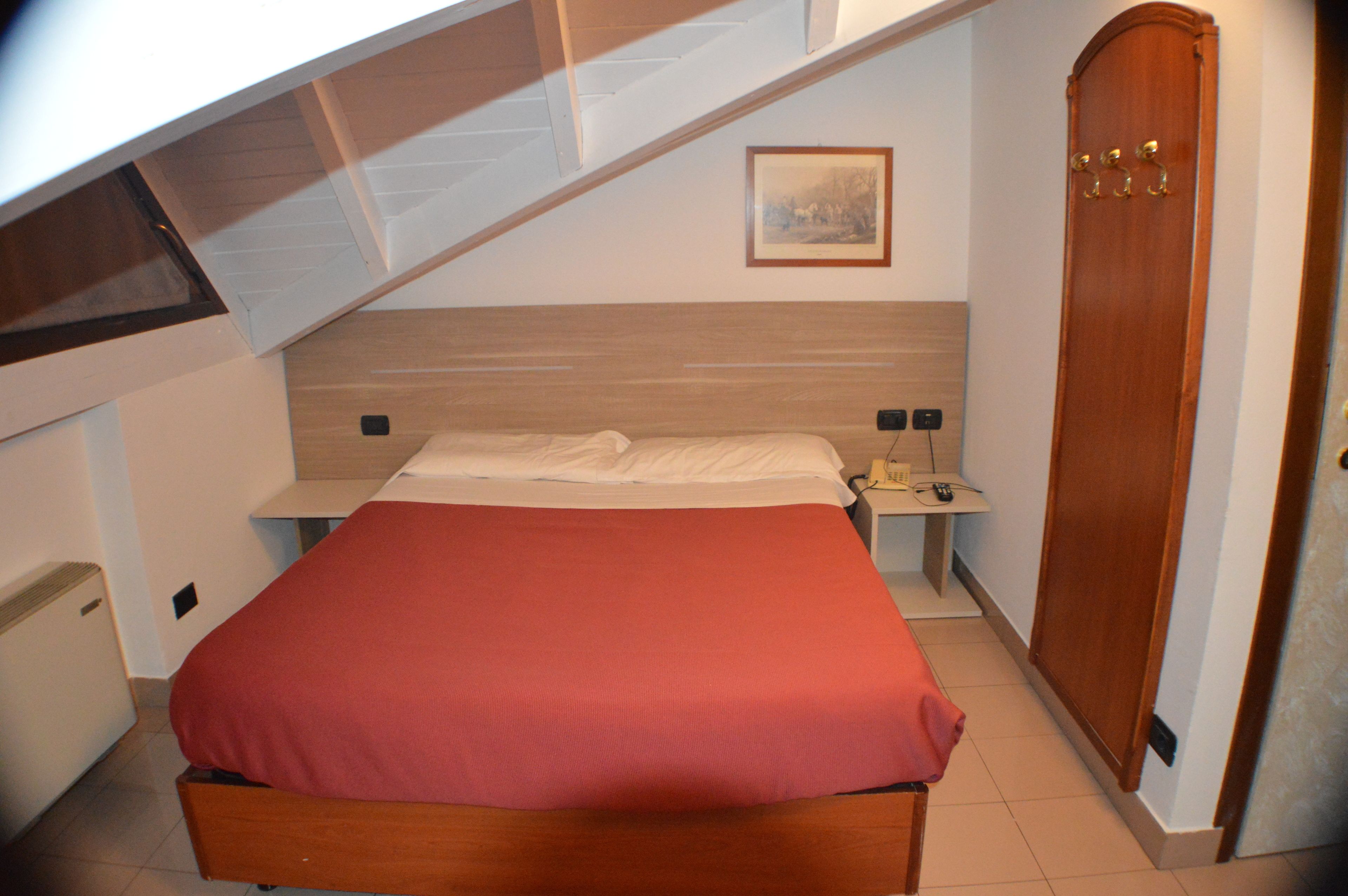 A bedroom with a bed, a nightstand, a bedside table, a wardrobe, and a painting on the wall.