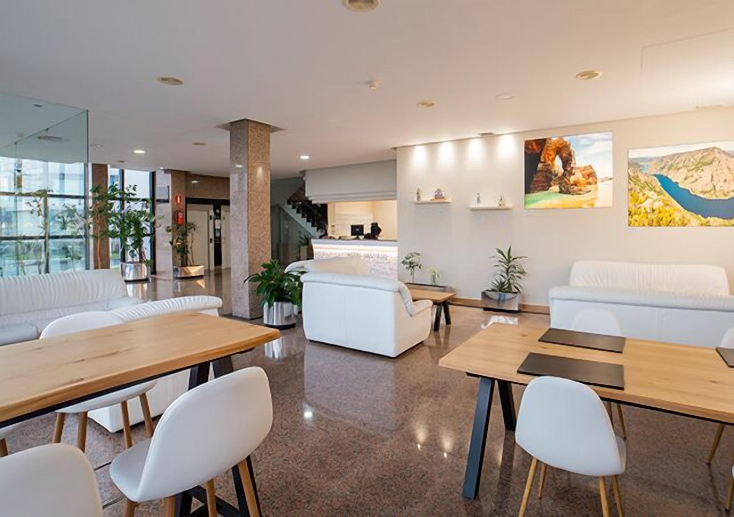 A modern hotel lobby with a reception desk, seating area, and a staircase leading to the upper floors.