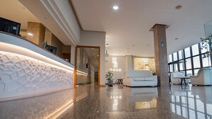 Un moderno vestíbulo de hotel con mostrador de recepción, zona de estar y grandes ventanales.
