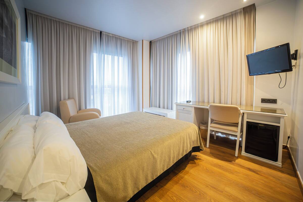 Een hotelkamer met een bed, een bureau, een stoel, een televisie en gordijnen.