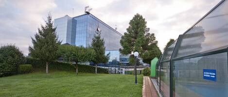 Un edificio moderno con fachada de vidrio, rodeado de un área verde bien cuidada y árboles.