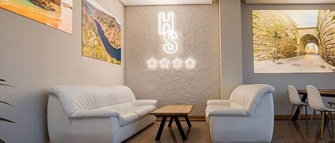 Un moderno vestíbulo de hotel con dos sofás blancos, una mesa de centro de madera y un aplique de pared que deletrea "HS".