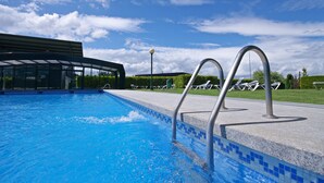 Una piscina con agua azul cristalina, escaleras de metal y sillas de descanso a un lado.