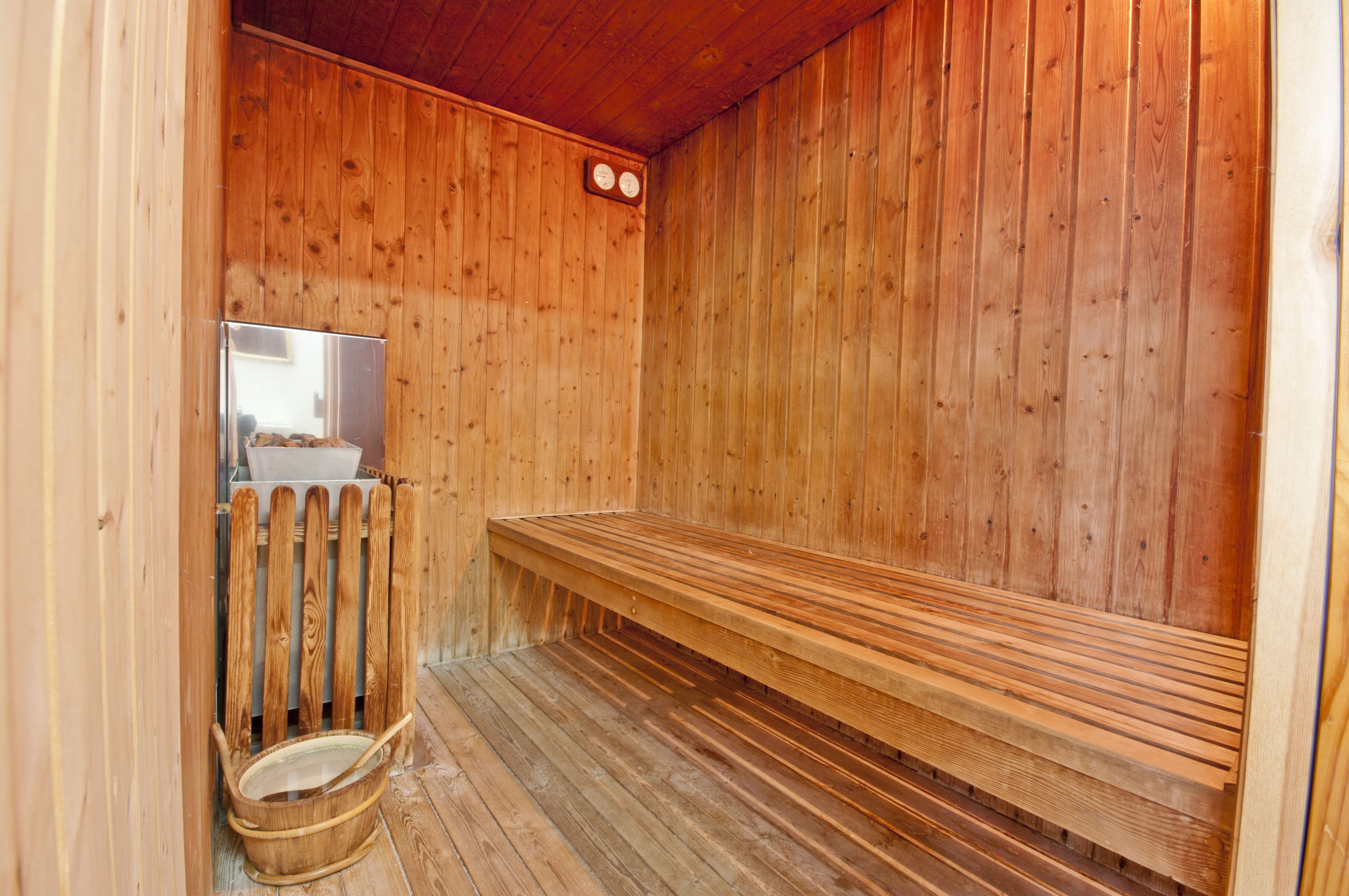 A wooden sauna with a bench, a wooden chair, and a small window.