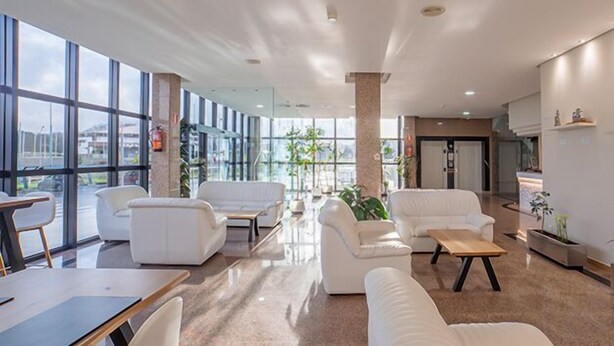 Un vestíbulo espacioso con sofás blancos, una mesa de centro de madera y amplias ventanas que ofrecen vistas de la ciudad.