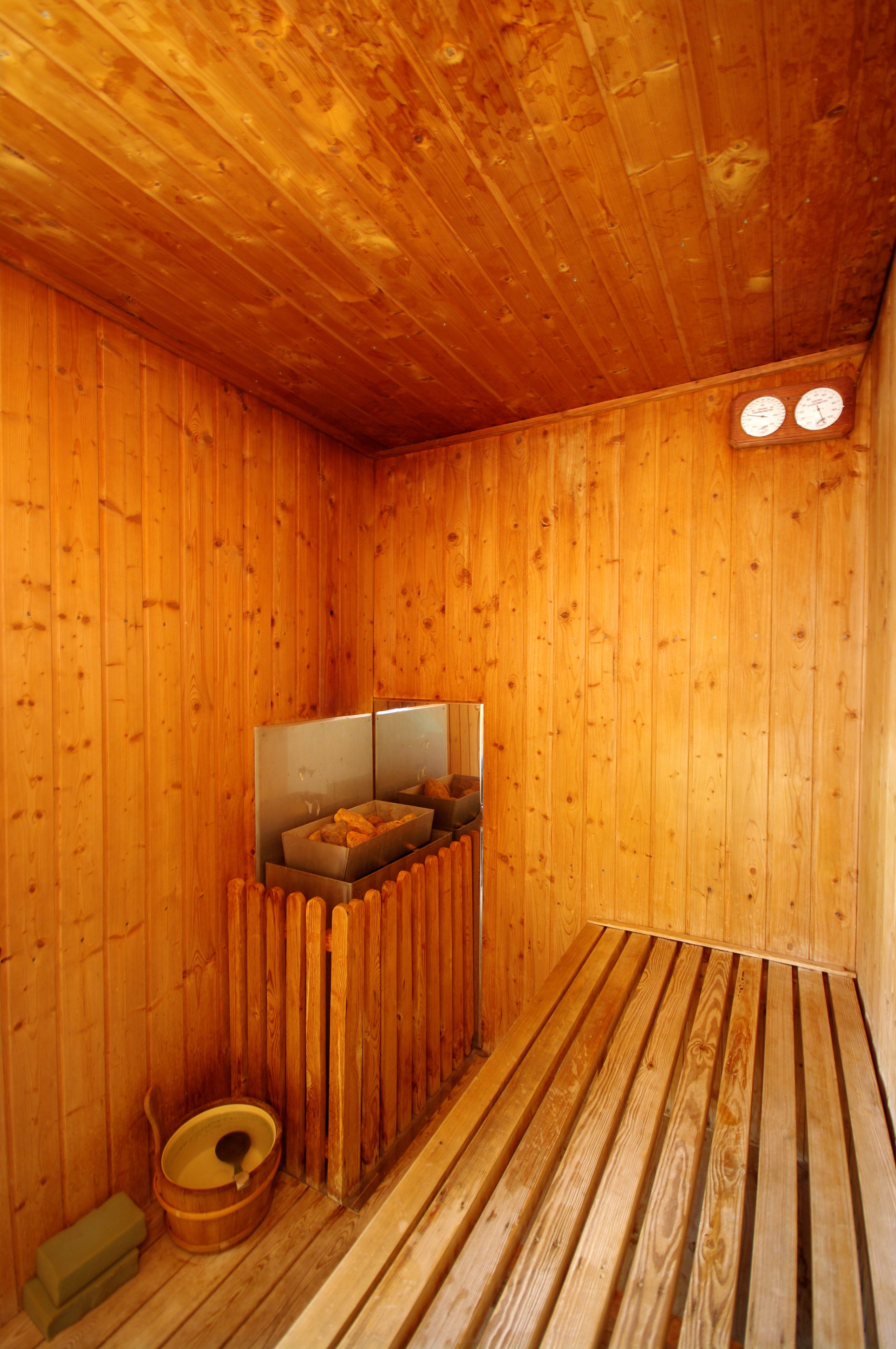 A wooden cabin interior with a wooden floor, a wooden bench, a wooden bowl, and a mirror on the wall.