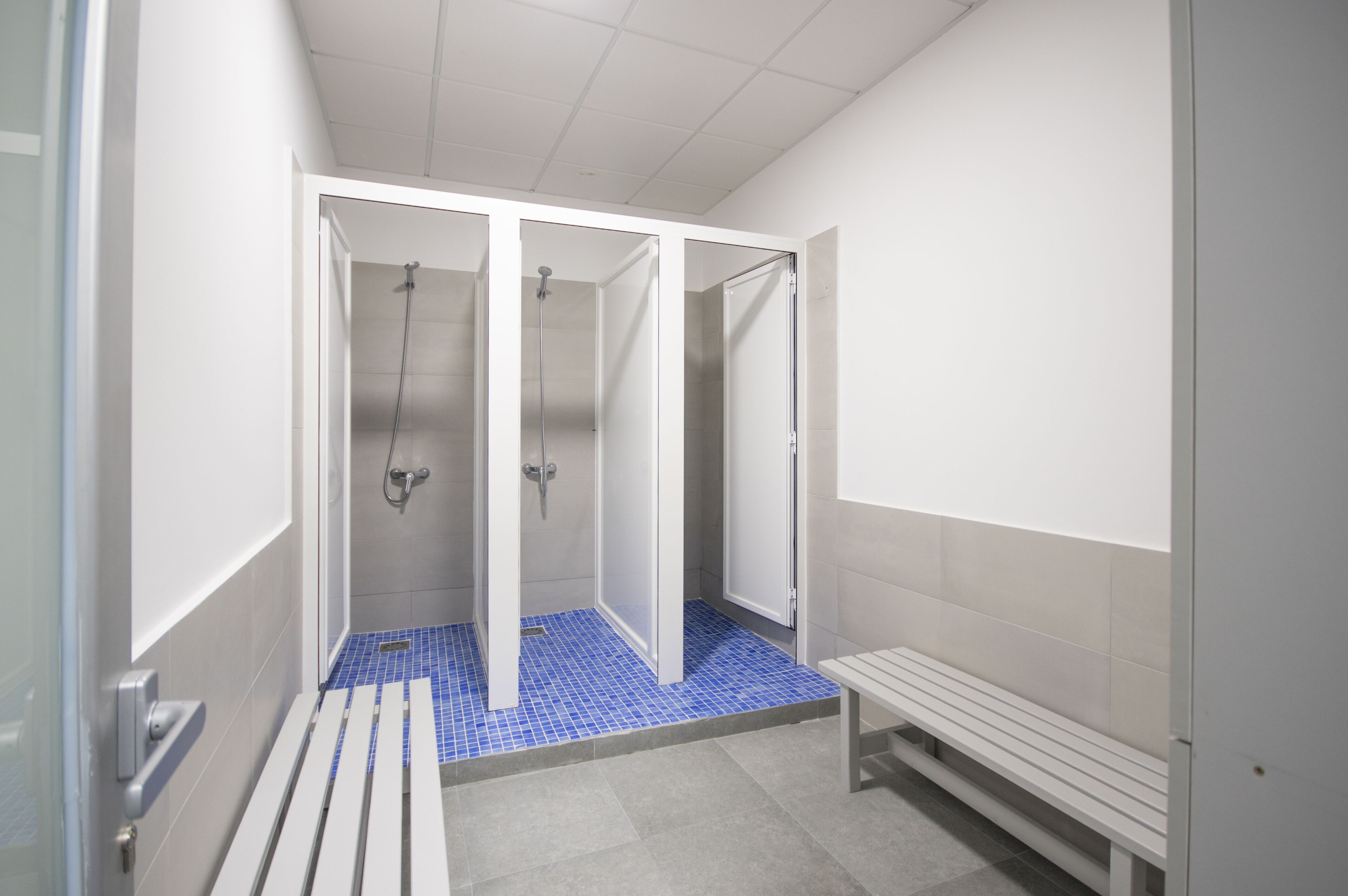 Un baño público con banco, zona de ducha y suelo de baldosas.