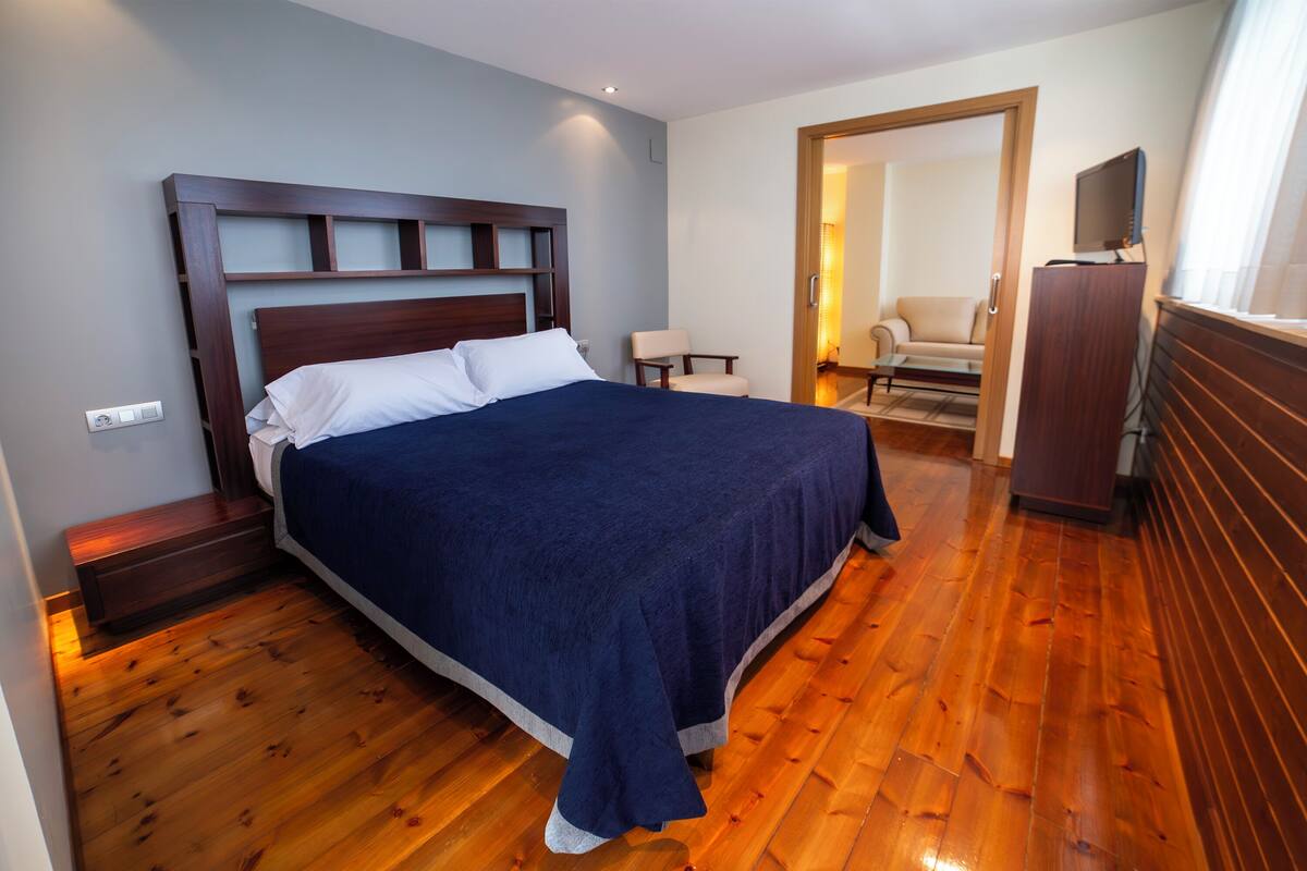 Een slaapkamer met een groot bed, houten vloeren, een bureau met stoel en een televisie op een kast.