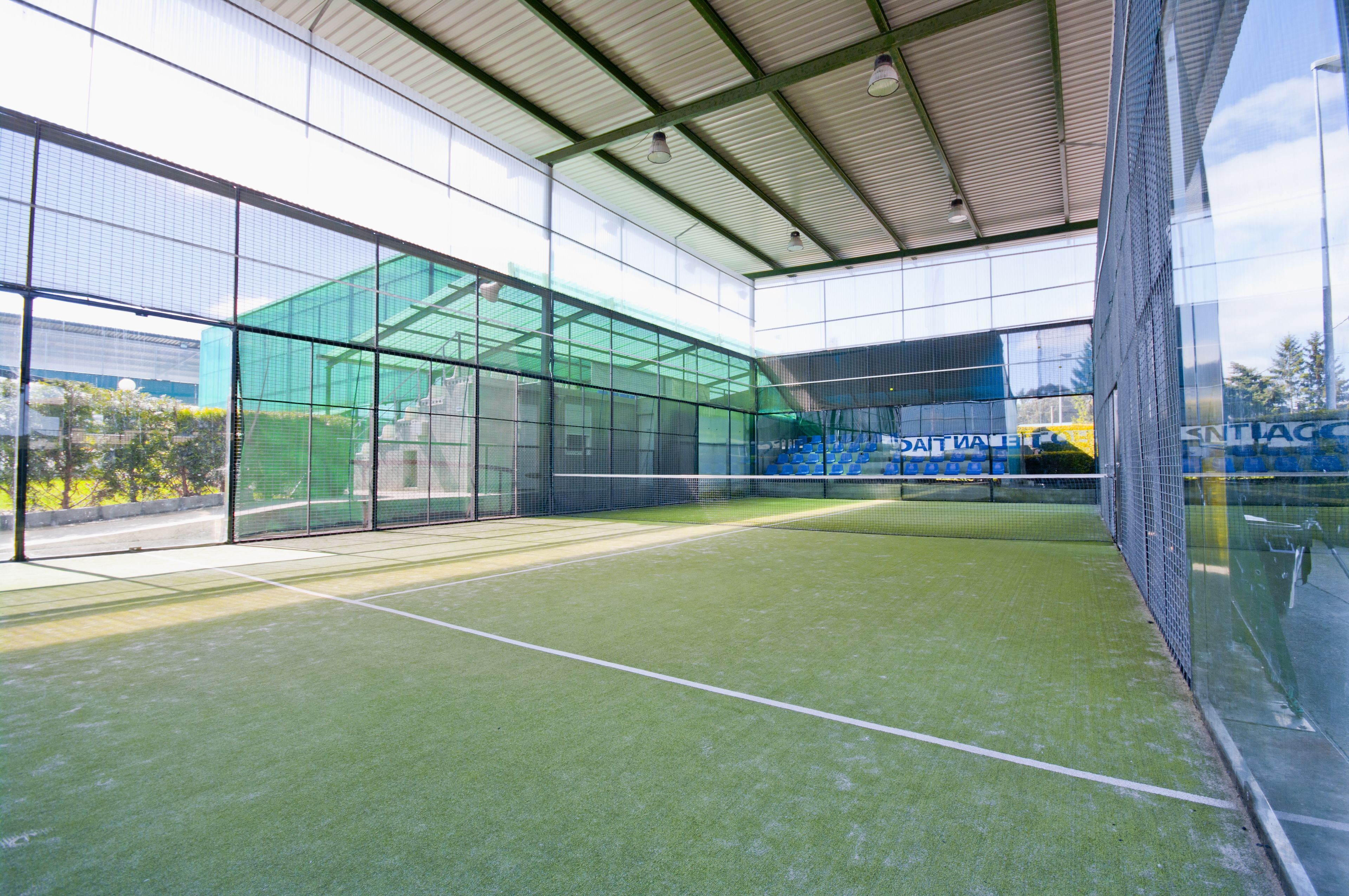 Un court de tennis intérieur avec des murs en verre, un toit et une surface en gazon synthétique.