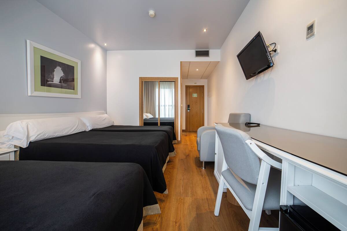 Een hotelkamer met twee bedden, een bureau, een stoel, een televisie en een deur die naar een andere kamer leidt.